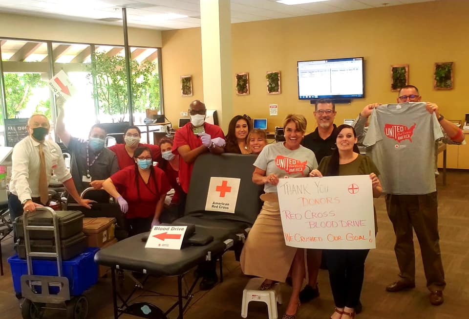 Group Of People In Office Holding Up Signs For Red Cross Blood Drive